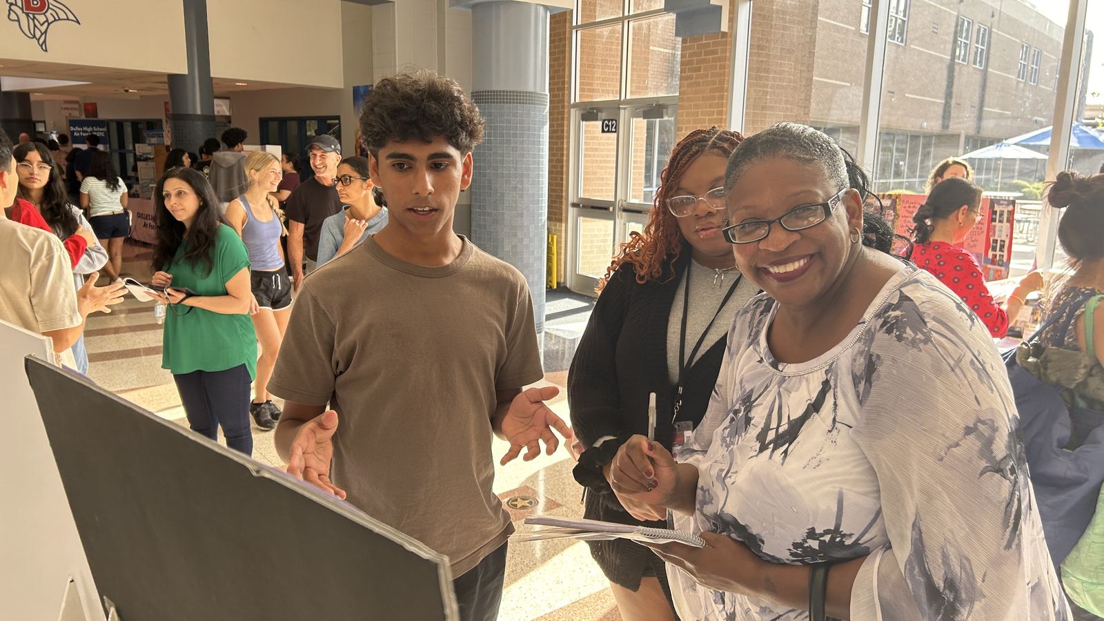 Trailblazers student explaining the Destination Imagination display board to a visitor